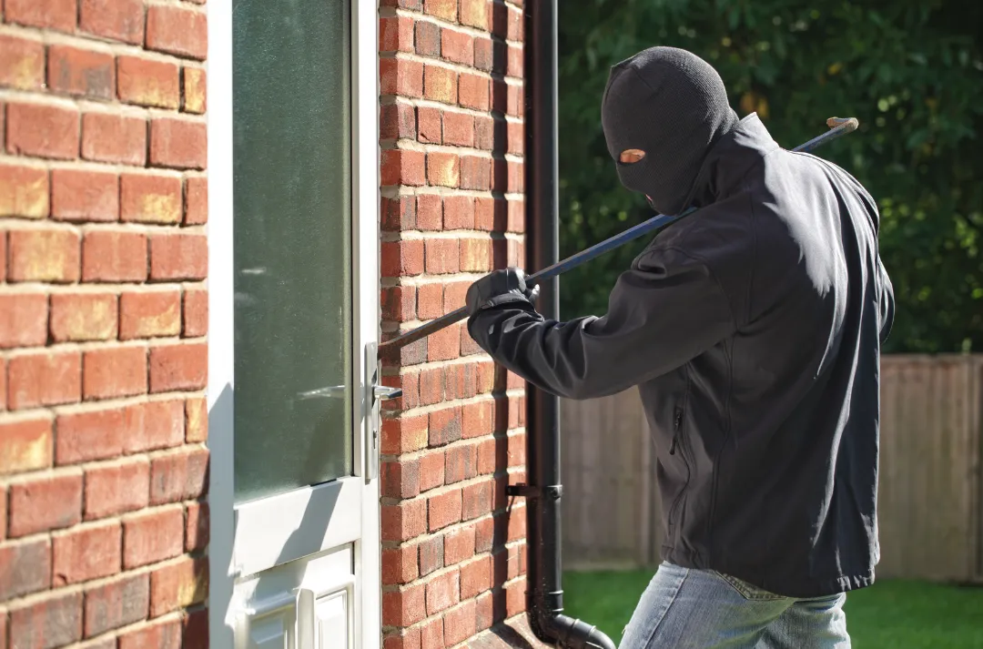 A person in dark clothing forcing a side door of a house